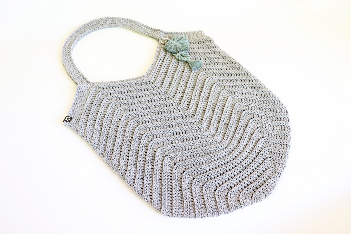 Flat-laid gray chevron crochet shoulder bag with integrated strap and tassel