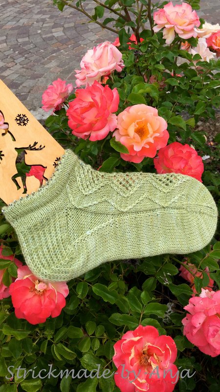 Hellgrüne gestrickte Damensocke mit Loch- und Rippenmuster auf rosa‑orange Rosen
