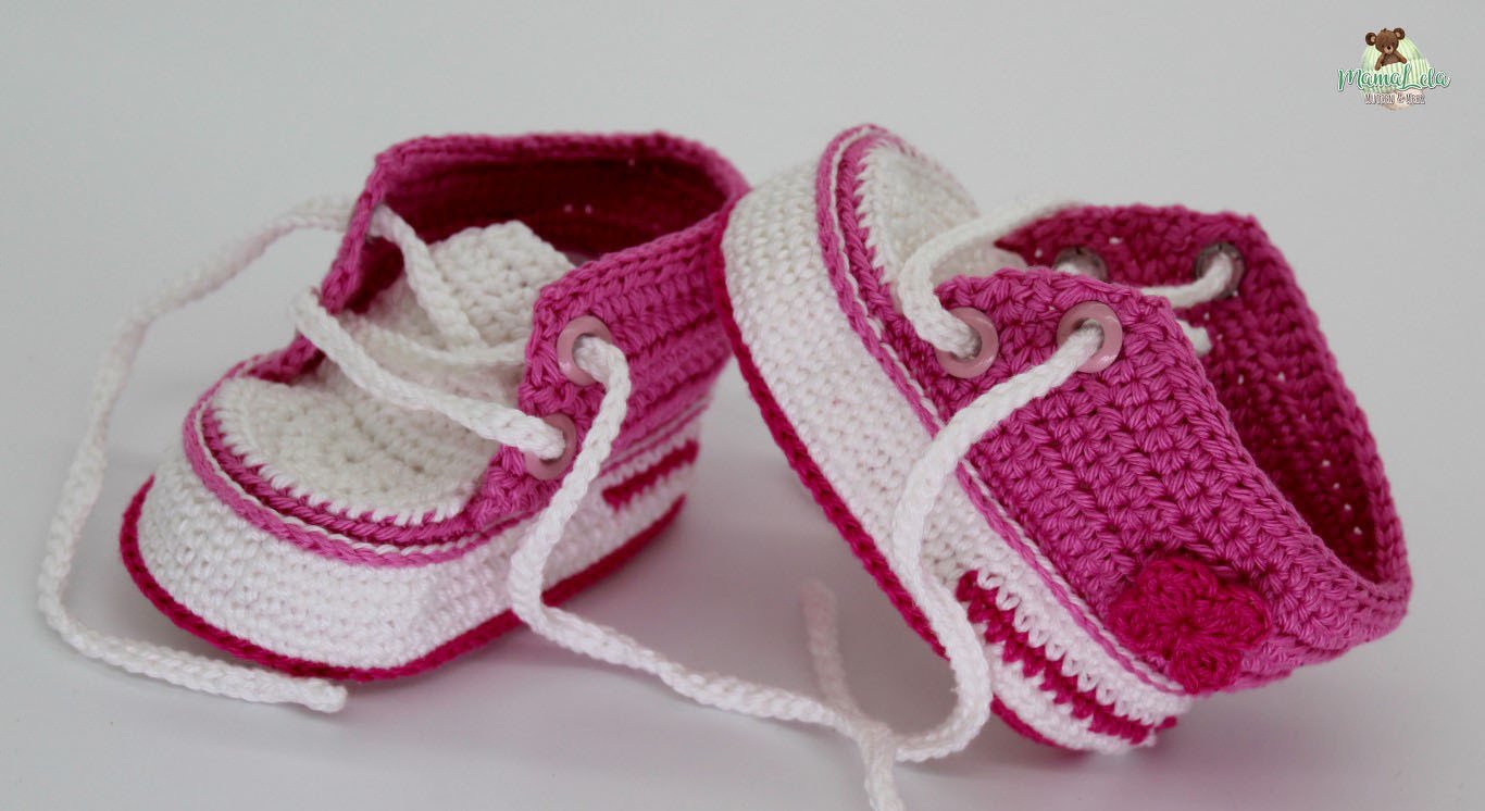 Zwei gehäkelte Babyschuhe in Pink und Weiß im Sneaker-Design mit Schnürsenkeln