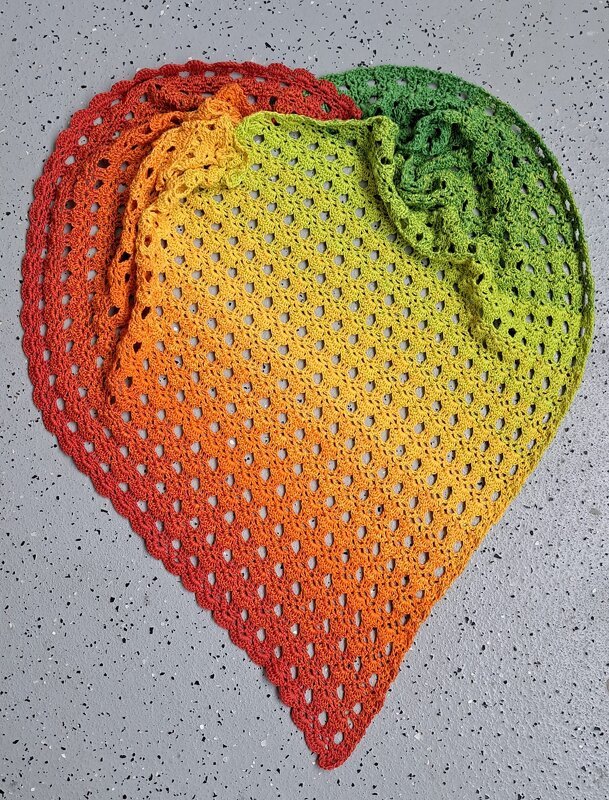 Gehäkeltes dreieckiges Tuch mit Verlaufsgarn in Grün, Gelb, Orange und Rot auf grauem Untergrund
