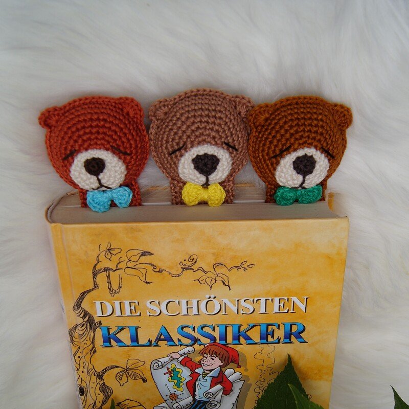 Drei gehäkelte Bären-Lesezeichen mit sichtbaren Maschenreihen und farbigen Fliegen