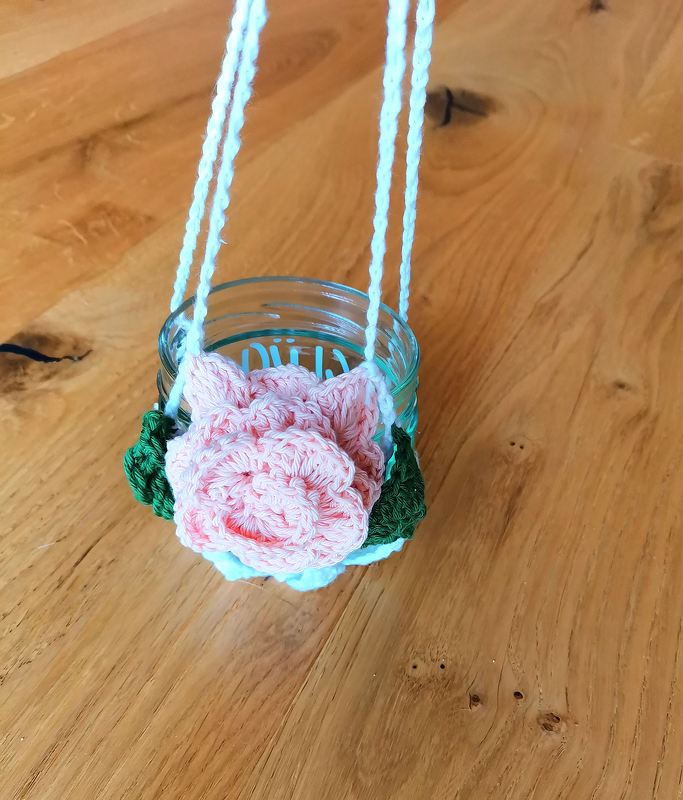 Glaswindlicht mit gehäkelter rosa Rose und grünen Blättern an weißem Band