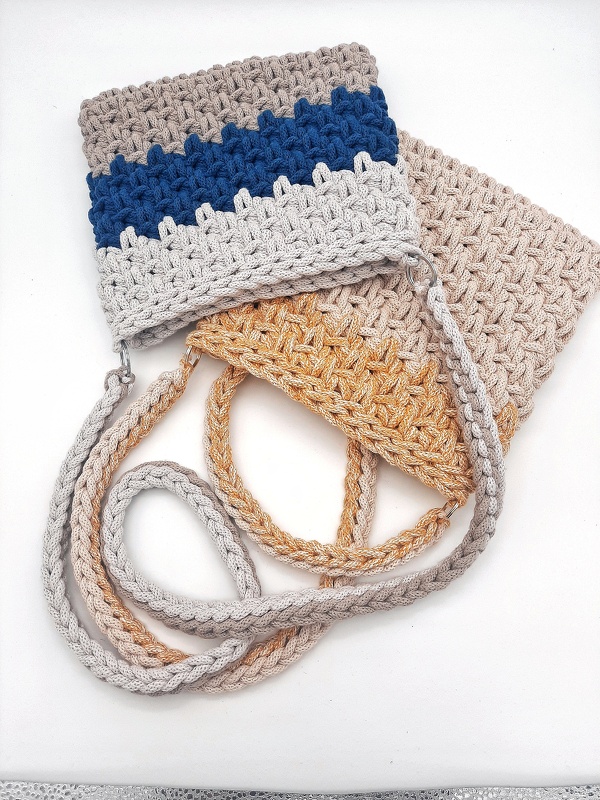 Rechteckige gehäkelte Umhängetasche mit blau-grauem Zickzackmuster und geflochtenem Trageriemen; gold-beige Tasche im Hintergrund.