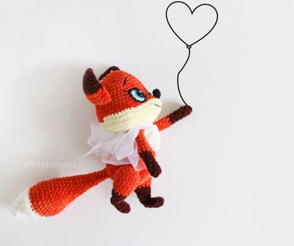 Handgehäkelter orange-weißer Amigurumi-Fuchs mit Tüllschleife und herzförmigem Ballon.