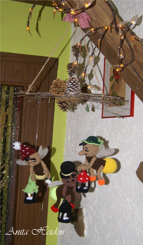 Drei gehäkelte Amigurumi-Glühwürmchen mit Hüten und Laternen an einem hängenden Zweig-Mobile