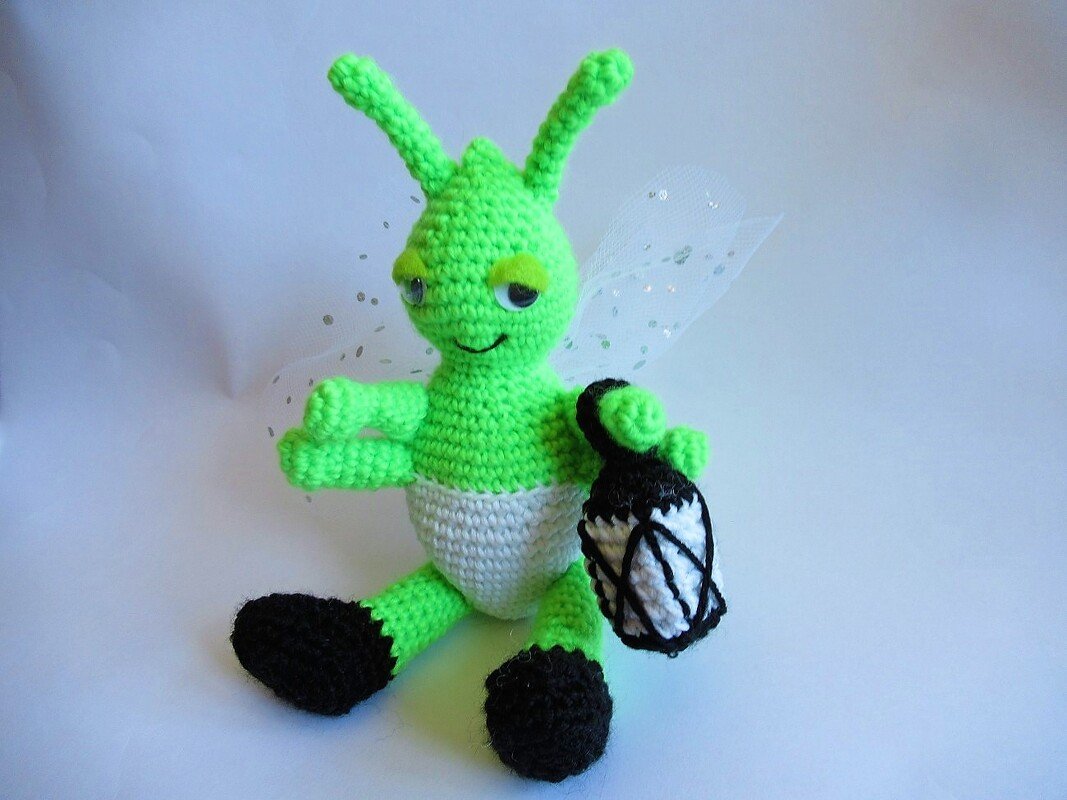 Gehäkeltes grünes Amigurumi-Wesen mit Fühlern, glitzernden Flügeln und kleiner Laterne