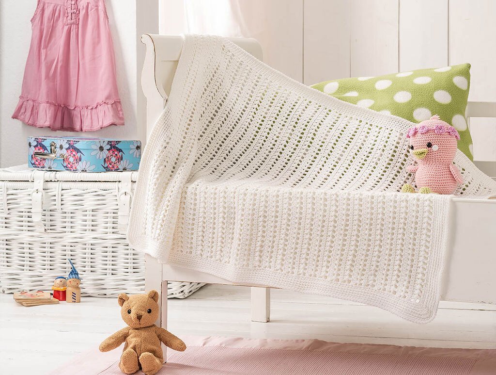 Weiße gehäkelte Babydecke mit Lochmuster auf einem Kinderbett