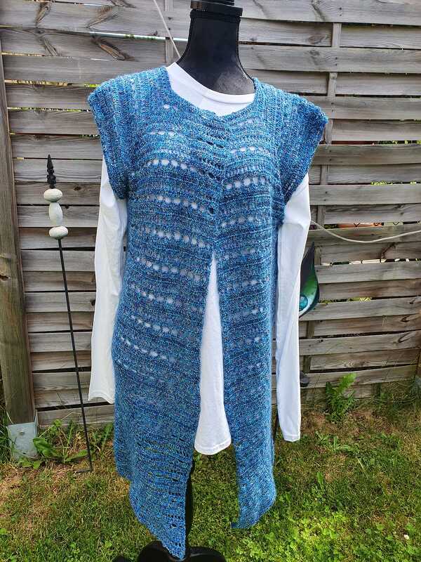 Lange gehäkelte blaue Weste mit Lochreihen auf Schaufensterpuppe über weißem Langarmshirt