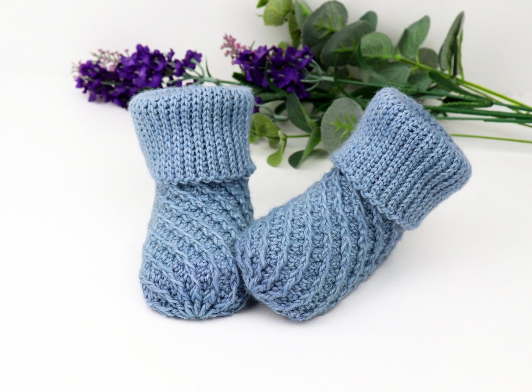 Light blue knitted baby booties with folded ribbed cuffs and diagonal textured stitch.