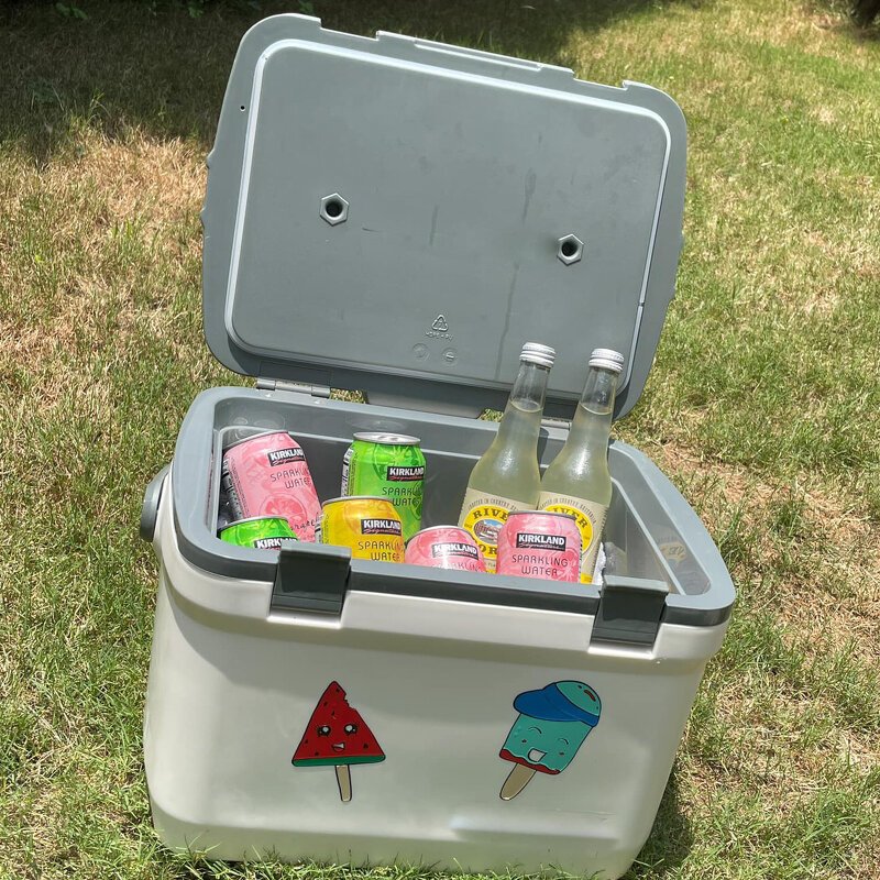 Geöffnete Kühltasche mit Dosen und Flaschen; vorne zwei bunte Aufkleber: Wassermelone und Eis am Stiel