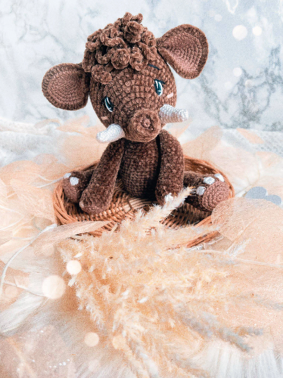 Braunes gehäkeltes Amigurumi-Wildschwein mit weißen Stoßzähnen im Körbchen, umgeben von Pampasgras