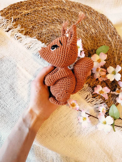Hand hält kleines braunes gehäkeltes Eichhörnchen-Amigurumi
