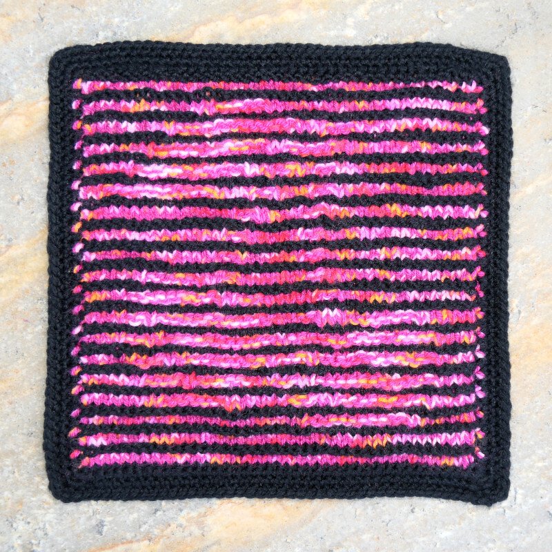 Quadratisches Strickstück mit pinken, orangen, gelben und schwarzen Streifen und schwarzem Rand