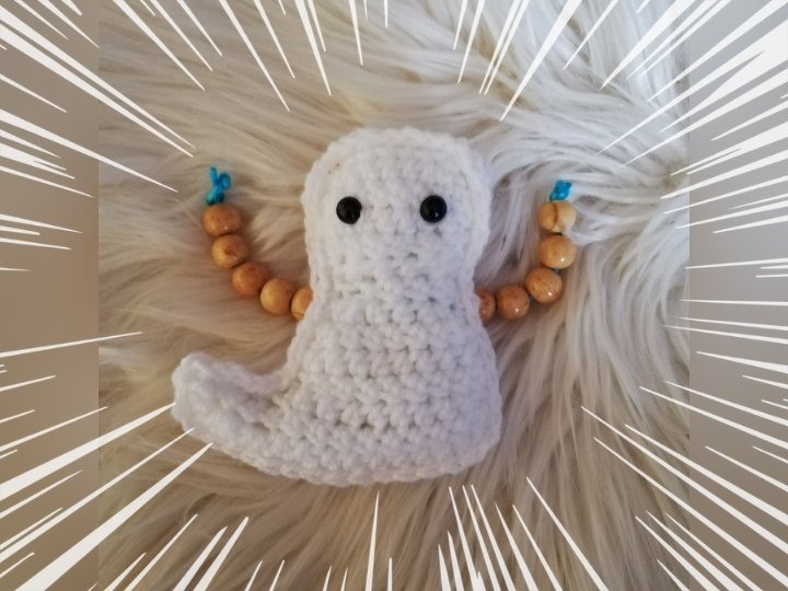 Weißer gehäkelter Amigurumi-Geist mit schwarzen Augen und Holzperlenarmen auf flauschigem Hintergrund