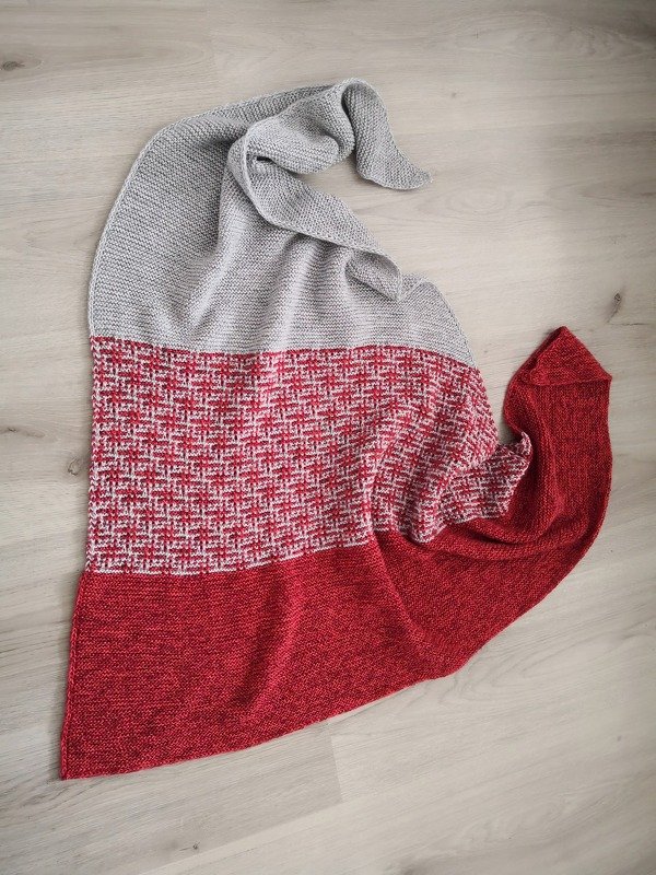 Gestricktes Dreieckstuch in Grau und Rot, liegend auf hellem Boden