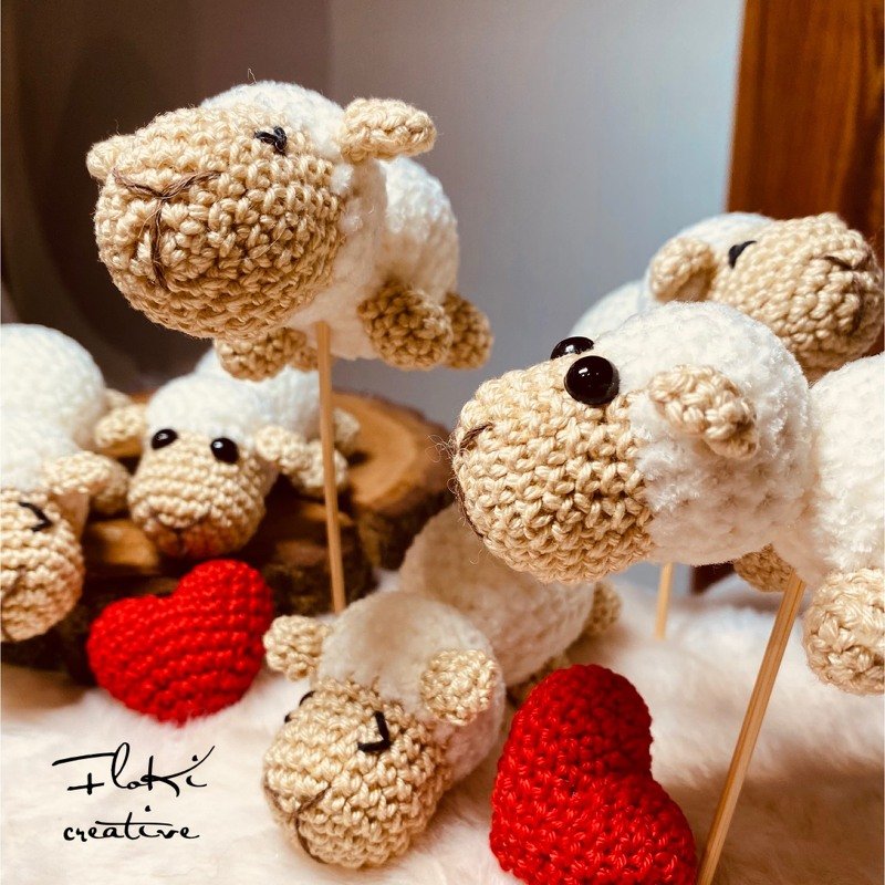 Mehrere kleine gehäkelte Amigurumi‑Schafe in Creme und Beige mit dunklen Augen und roten Häkelherzen