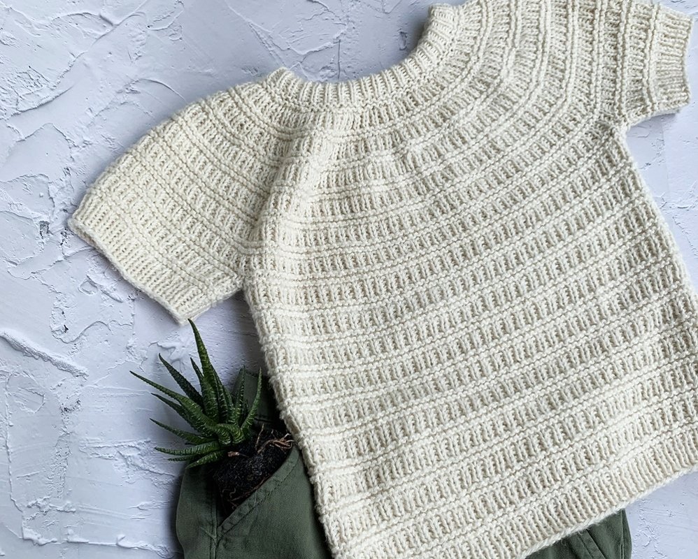 Nahaufnahme eines kurzärmligen Kinderpullovers in Creme mit deutlicher Rippenstruktur