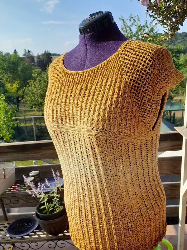 Senfgelbe, handgehäkelte Damen-Tunika mit Rippen- und Lochmuster auf einer Schneiderpuppe im Freien.