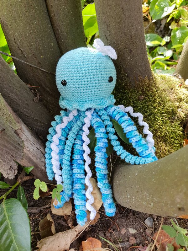 Gehäkelte blaue Qualle-Amigurumi mit spiralförmigen blau-weißen Tentakeln und weißer Schleife