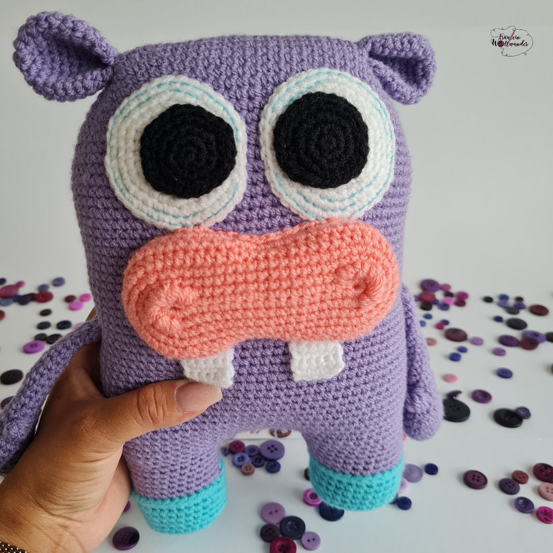 Lila gehäkeltes Amigurumi-Nilpferd mit rosa Schnauze und großen Augen, von einer Hand gehalten