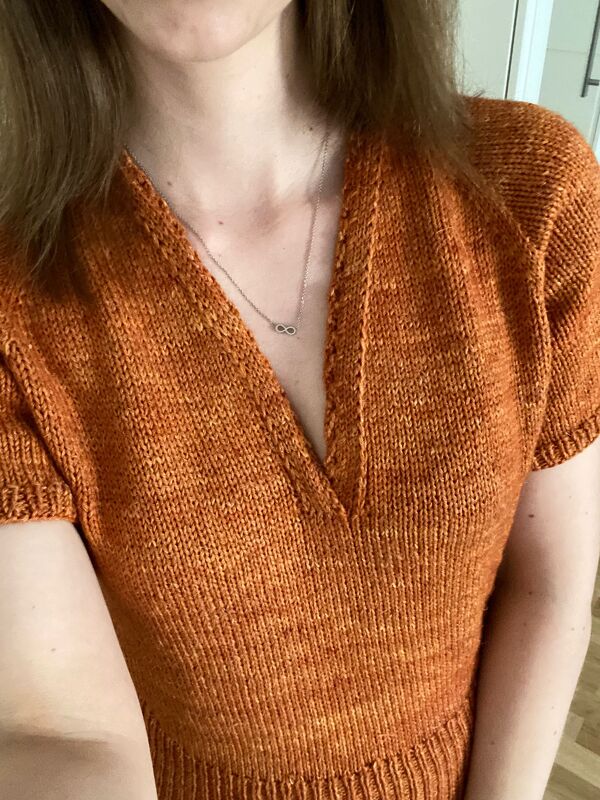 Close-up of rust-colored short-sleeve V-neck sweater showing stockinette stitch and ribbed hem
