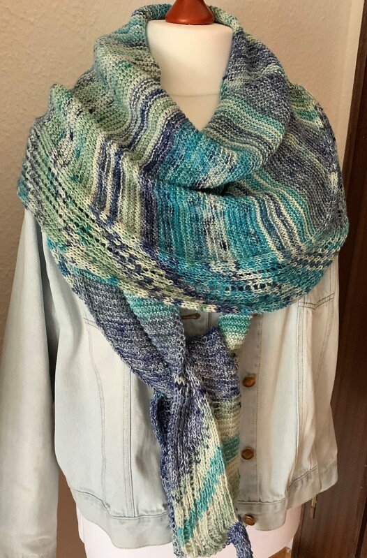 Gestricktes Dreieckstuch in Blau, Türkis und Grün mit Lochmuster, drapiert über eine helle Jeansjacke an einer Schaufensterpuppe