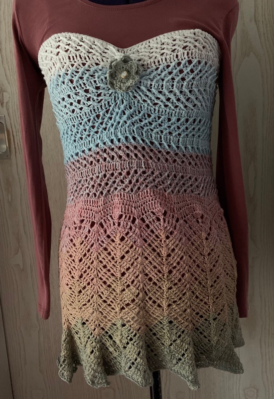Gehäkeltes Bandeau-Top in Pastell-Farbverlauf mit Spitzendetails und Blumenapplikation auf einer Schaufensterpuppe.