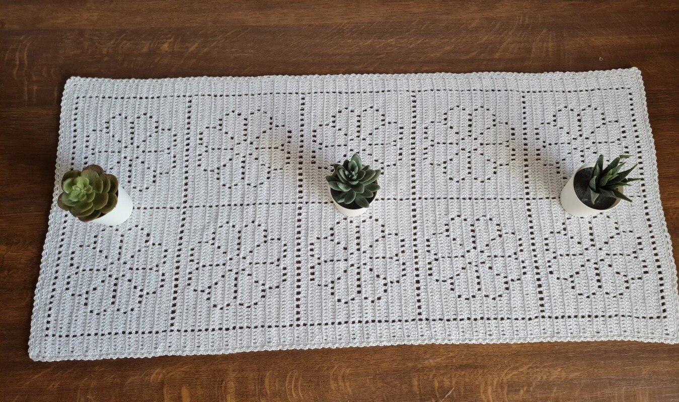 Weiß gehäkelter Tischläufer im Filetmuster mit Blumenmotiven auf Holztisch, dekoriert mit drei kleinen Sukkulenten