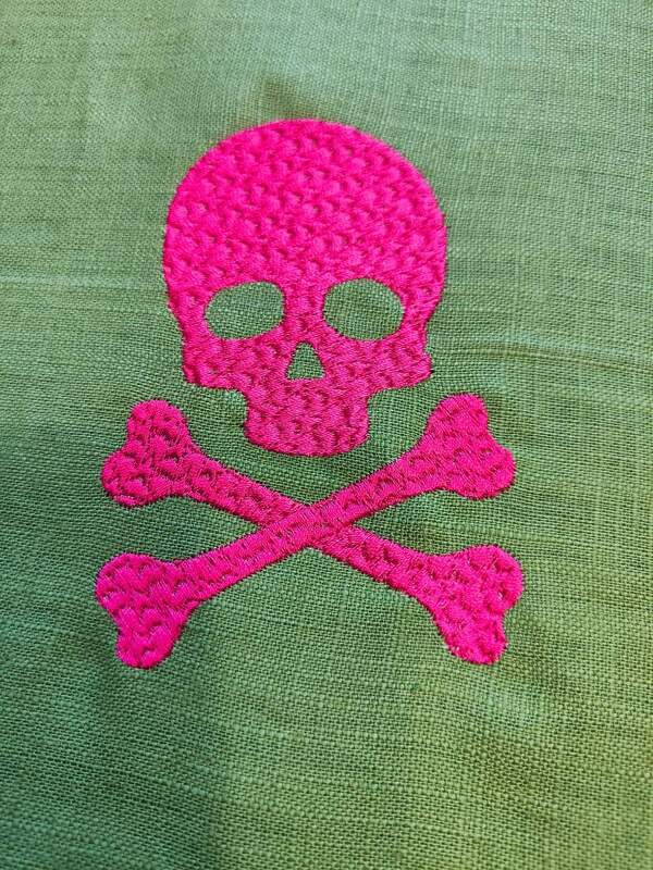 Gestickter pinker Totenkopf mit gekreuzten Knochen auf grünem Stoff