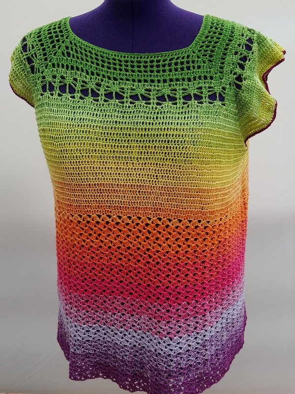 Gehäkeltes Damen-Top in Regenbogenfarben auf einer lila Schneiderpuppe.