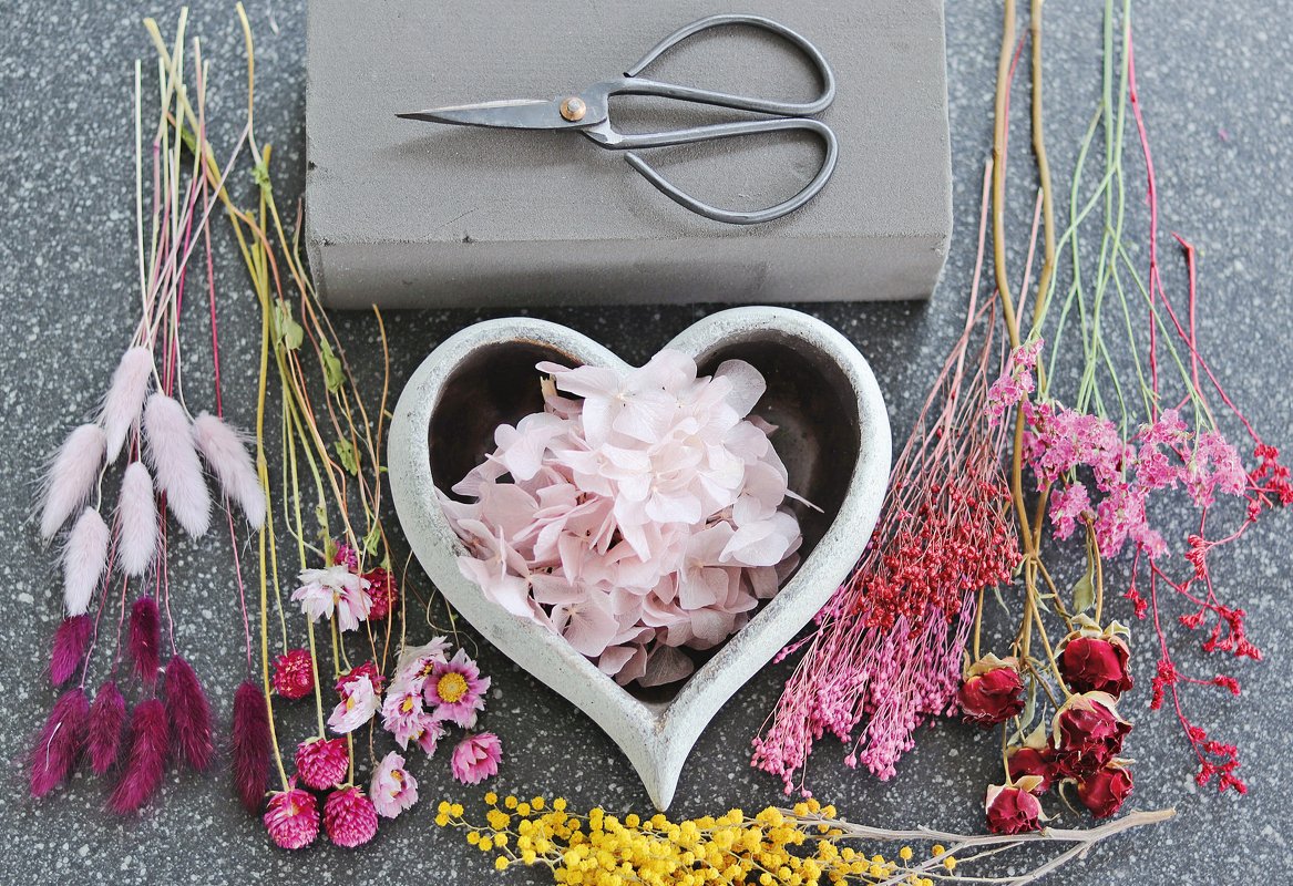 Kreative Anordnung von Trockenblumen, herzförmiger Schale mit Blüten, Schere und Bastelzubehör