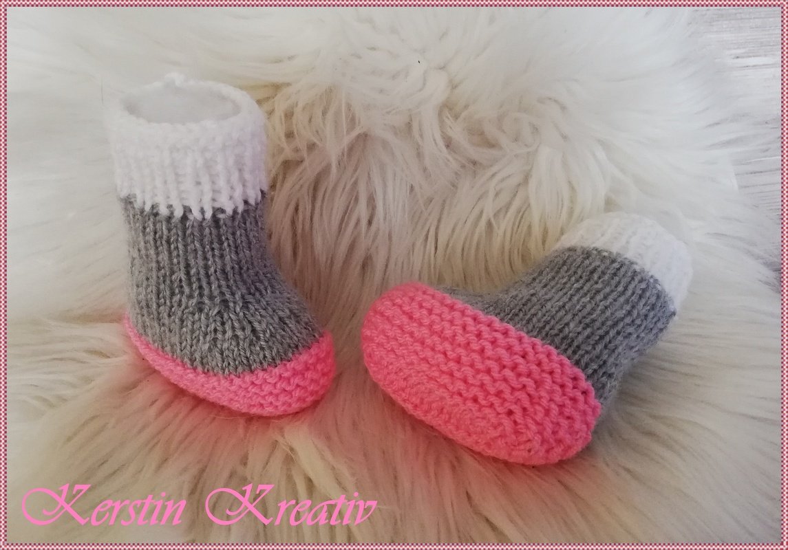 Zwei niedliche gestrickte Babyschuhe grau, weiß und pink auf weißem Fell