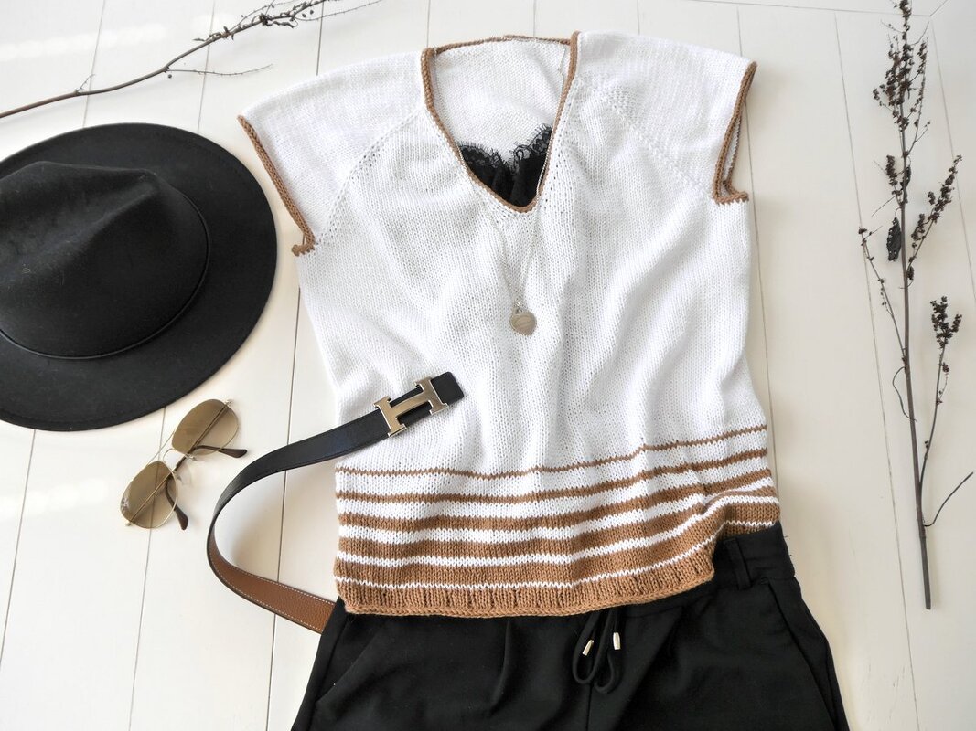 Weißes gestricktes ärmelloses Top mit braunen Streifen und V-Ausschnitt, flach gelegt neben einem Hut, einer Sonnenbrille und einem schwarzen G
rtel.