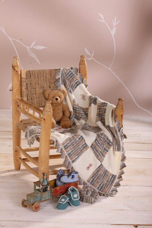 Holzstuhl mit karierter Babydecke, Teddybär, Spielzeug-Lkw und zwei Paar Babyschuhe auf hellem Boden.