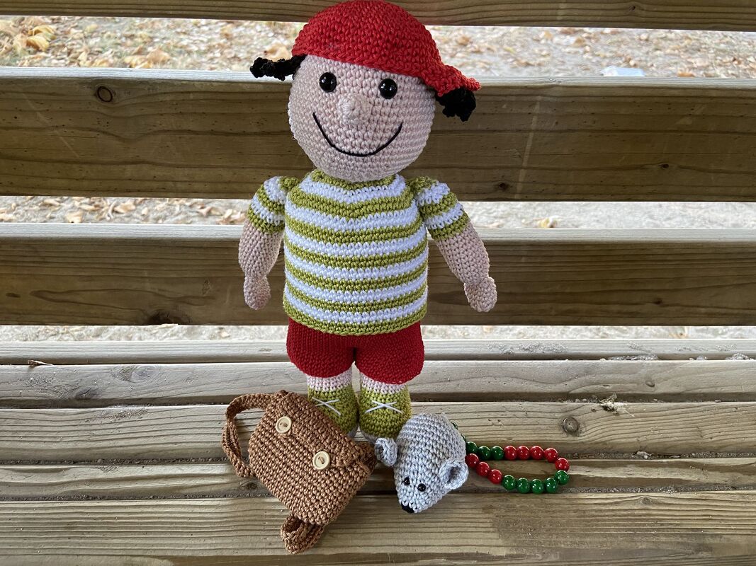 Gehäkelte Amigurumi-Jungenpuppe mit roter Kappe, gestreiftem Shirt, braunem Ranzen und kleiner Maus auf Holzstufen