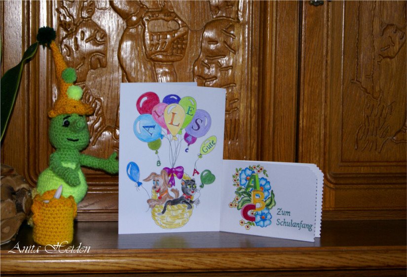 Zwei Papierkarten: eine kleine Karte mit ABC-Ausmalmotiv 'Zum Schulanfang', eine größere Karte mit bunten Ballons und Tierillustration; links eine gehäkelte Puppe