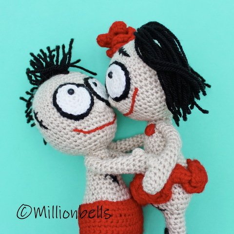 Two amigurumi crochet dolls hugging against a teal background.