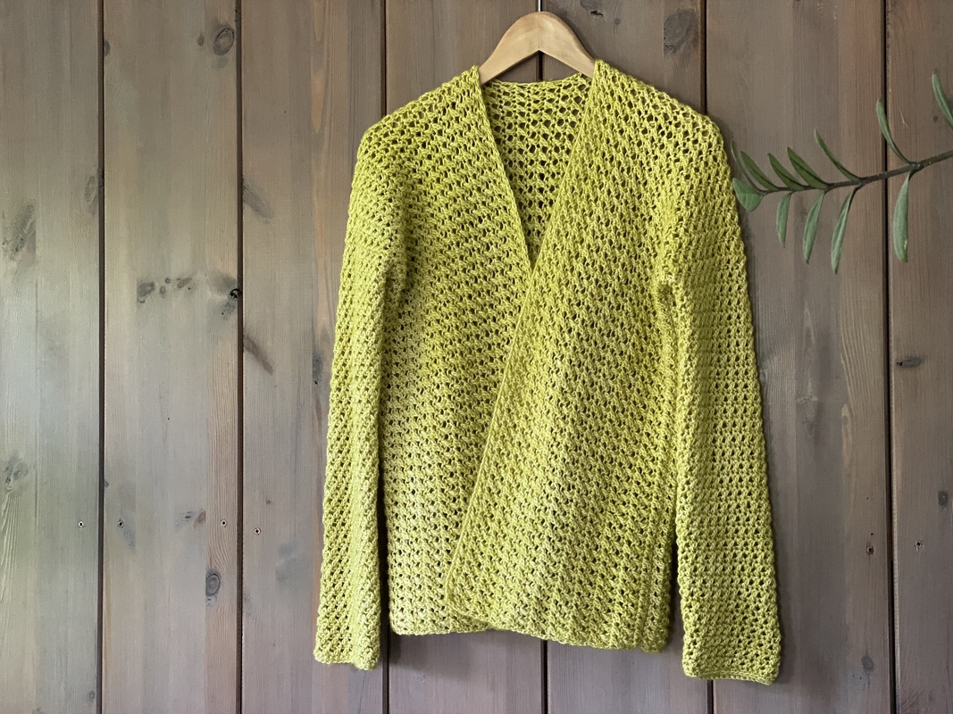 Lime-green open-front crochet cardigan with V-neck and long sleeves hanging on wooden hanger