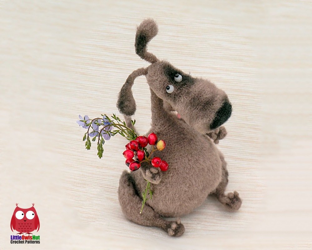 Brown crocheted amigurumi dog plush with floppy ears holding red berries and small purple flowers.