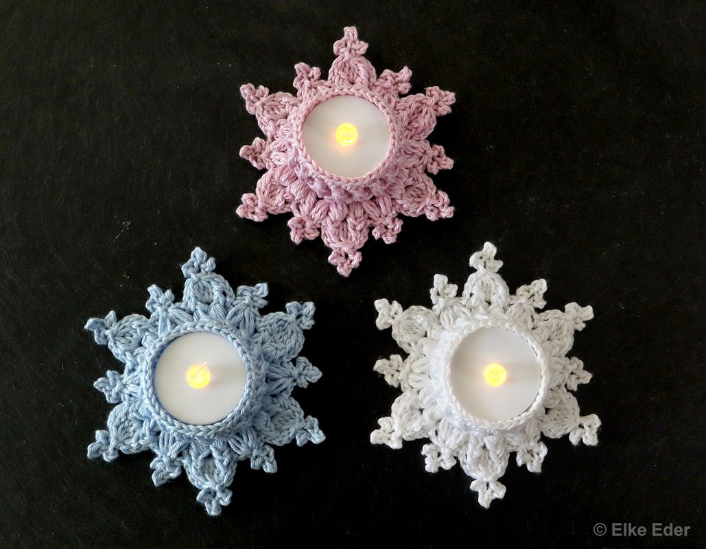 Three crocheted snowflake tealight holders in pink, blue, and white with LED lights.