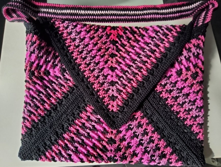 Handgehäkelte Umhängetasche in Pink und Schwarz mit diagonalem Muster und gehäkeltem, gestreiftem Riemen.
