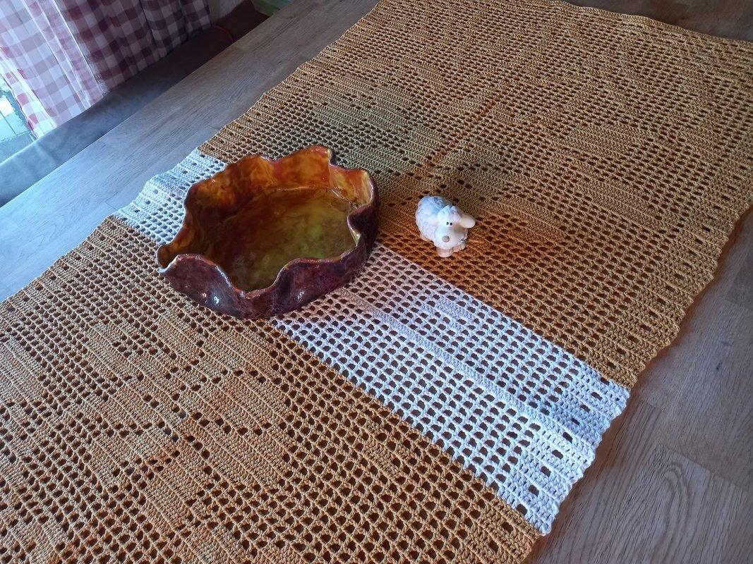 Ockergelber Häkel-Tischläufer im Filet-Muster mit weißem Streifen, Keramikschale und Schaffigur auf Holztisch