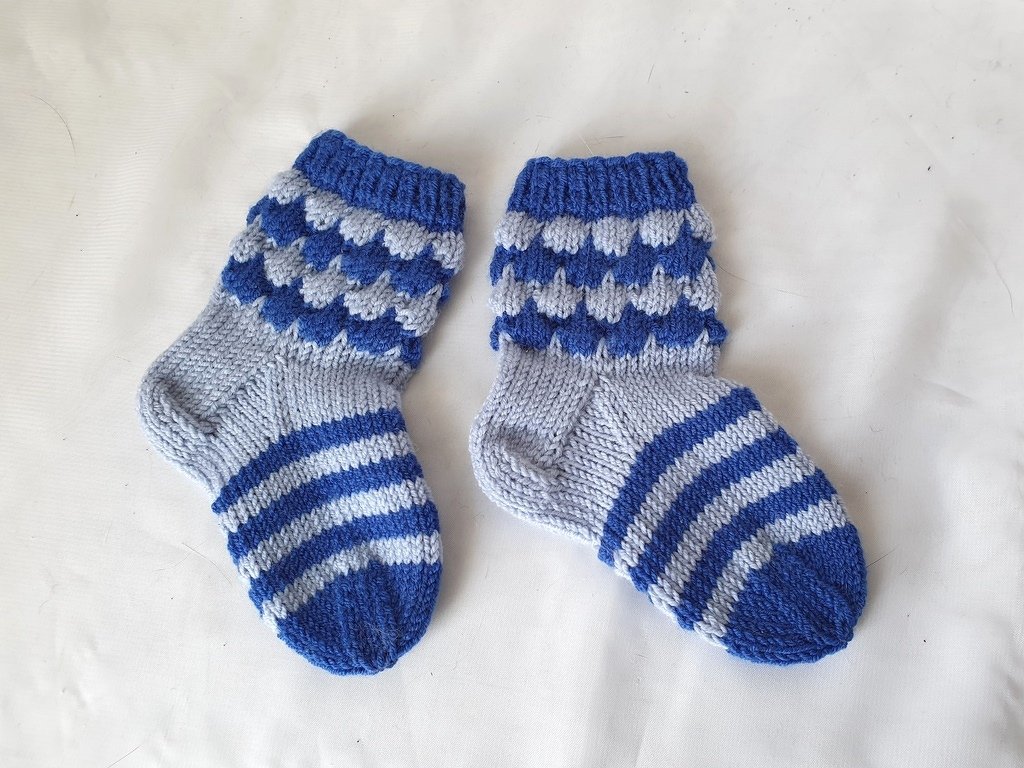 Gestrickte Babysocken mit Streifen am Fuß und Muschelmuster am Schaft auf weißem Hintergrund