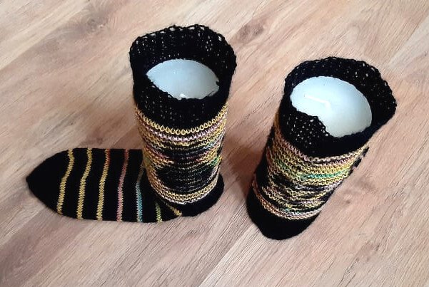 Gestrickte Socken und Stulpen mit mehrfarbigen Streifen, schwarzem Bündchen und Spitzenkante, teils auf Formen, teils flach auf Holzboden