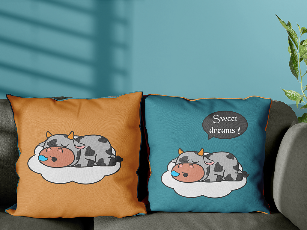 Zwei Kissen auf Sofa mit demselben Kuh-auf-Wolke-Motiv; linkes Kissen orange, rechtes türkis mit Sprechblase 'Sweet dreams!'