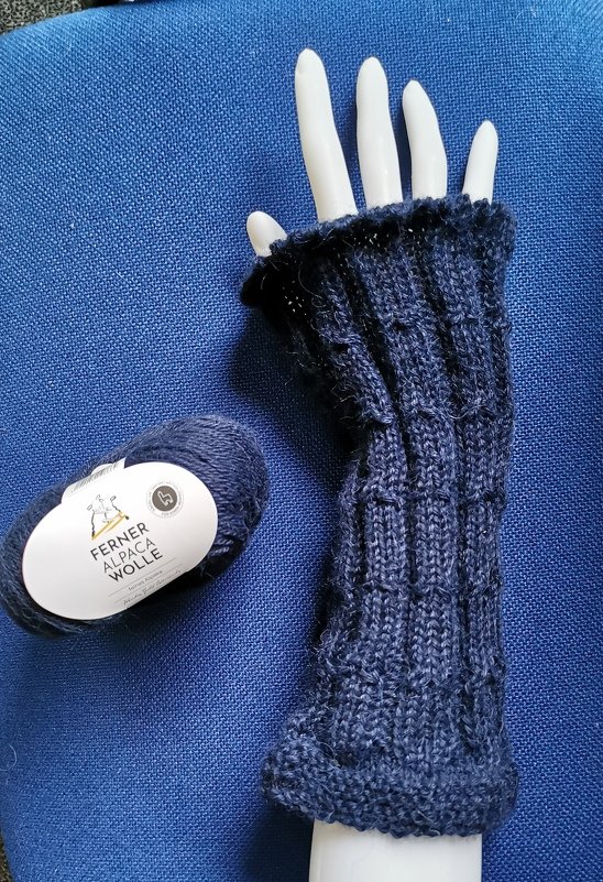 Dunkelblaue, fingerlose Armstulpe auf weißer Schaufensterhand mit Garnknäuel daneben