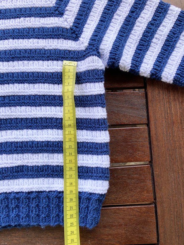 Gestrickter Kinderpullover in Blau-Weiß mit Maßband auf Holztisch