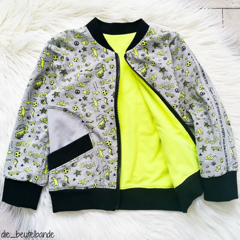 Flachliegende Kinderjacke mit durchgehendem Reißverschluss, aufgesetzter Tasche und leuchtendem Innenfutter