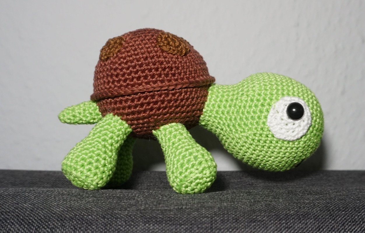 Side view of a green-and-brown crocheted turtle amigurumi with rounded shell and four legs