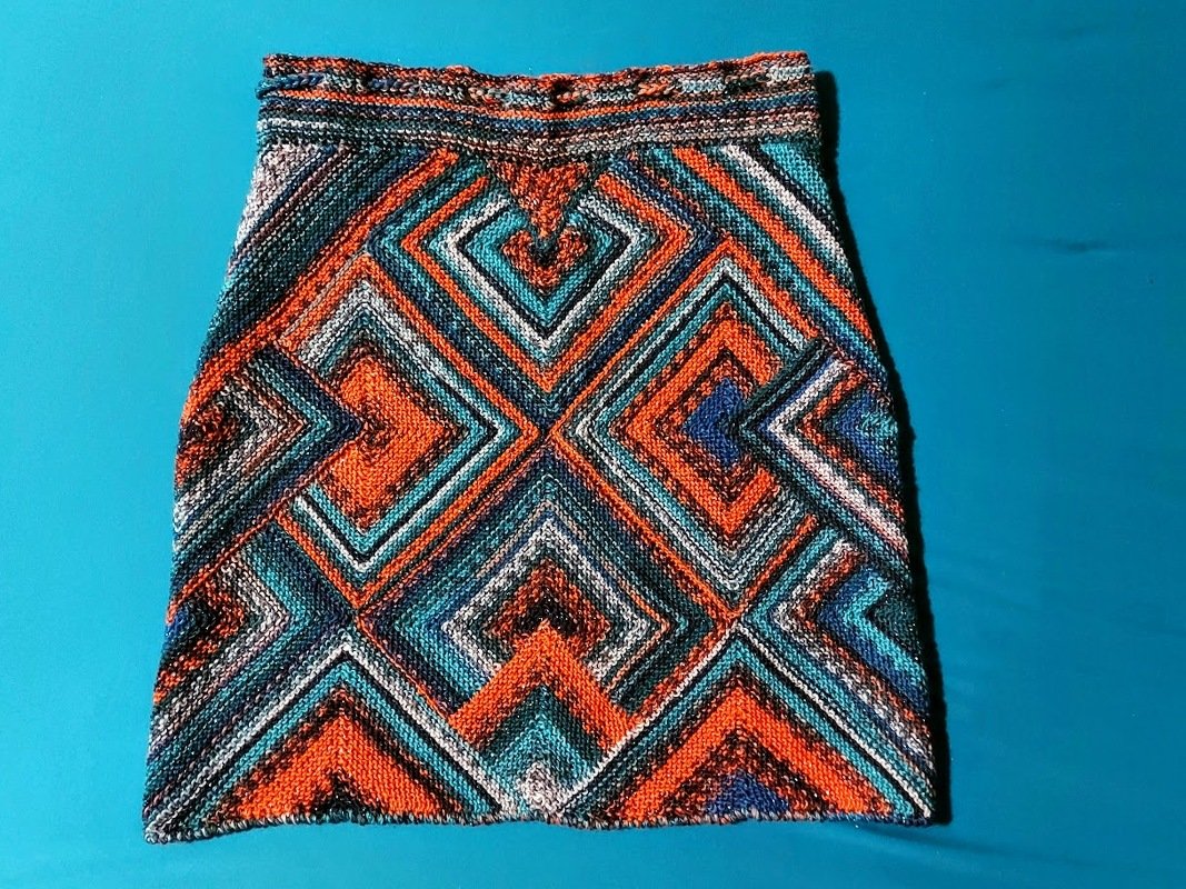Gestrickter Damenrock mit geometrischem Rautenmuster in Orange, Türkis und Blau auf blauem Untergrund